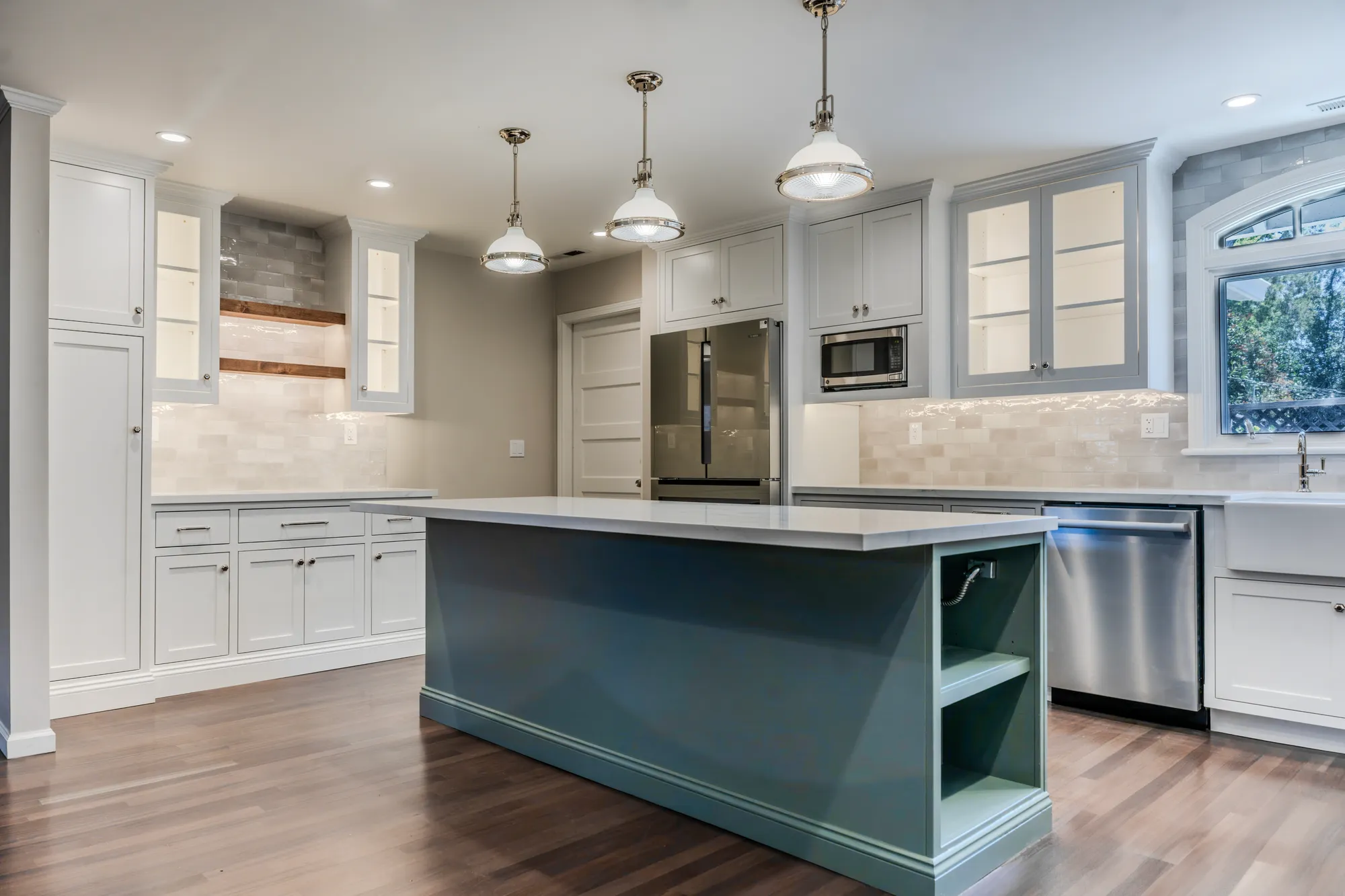 Remodeled kitchen with a teal island, white shaker cabinets, glass-front uppers and nickel pendants, built by EDL Construction